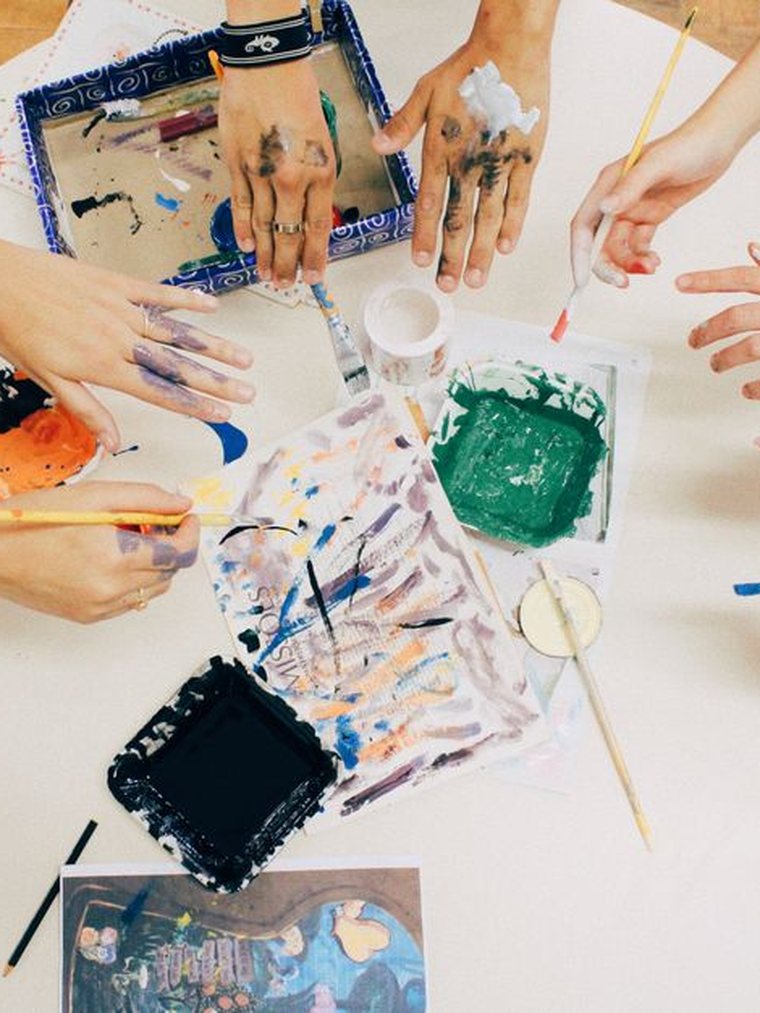 Mains autour d'une table couverte de peintures et d'outils créatifs